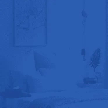 A minimalist bedroom with a bed, framed wall art, and a small plant, all covered in a monochromatic blue color wash.
