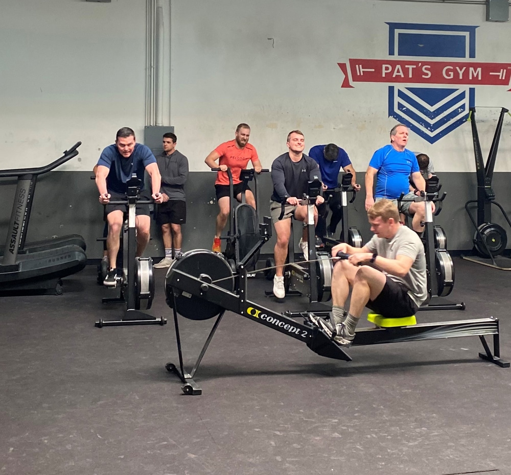 Men training on rowing machines and air bikes during a group fitness class at Pat's Gym.