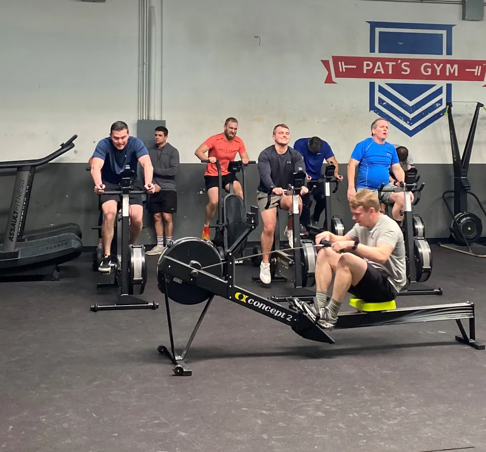 Men training on rowing machines and air bikes during a group fitness class at Pat's Gym.