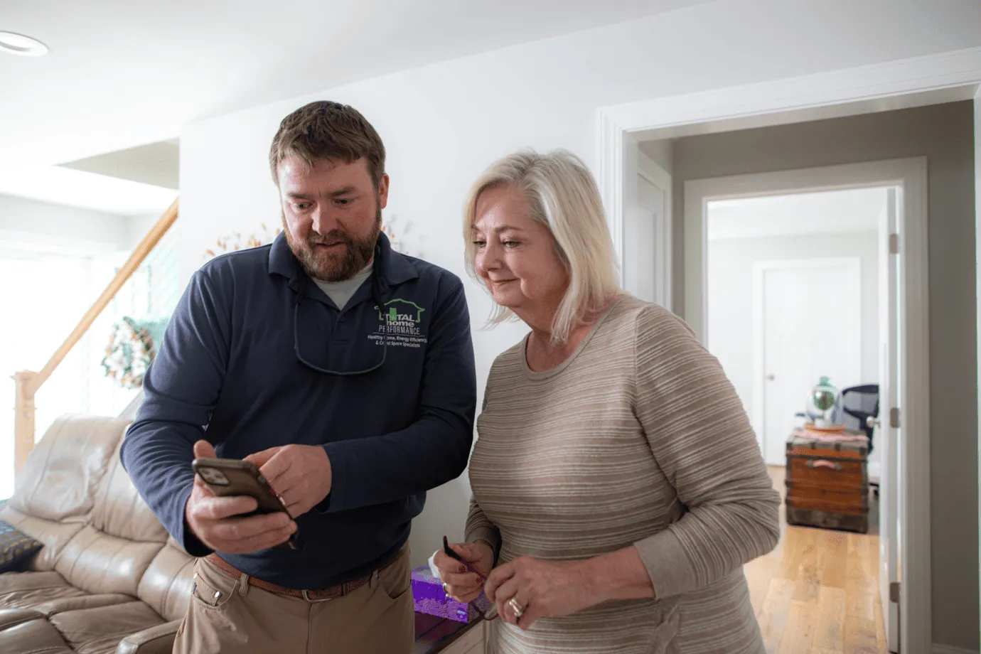 An HVAC professional shows information on a smartphone to a woman during a home service consultation
