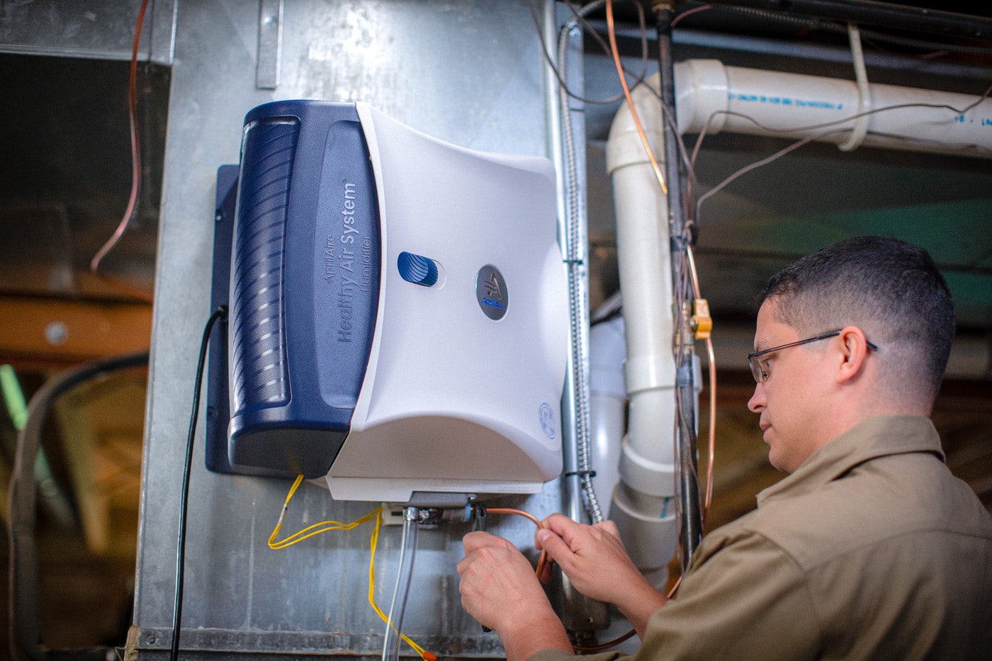A technician installs an AprilAire Healthy Air System humidifier onto a home furnace unit.