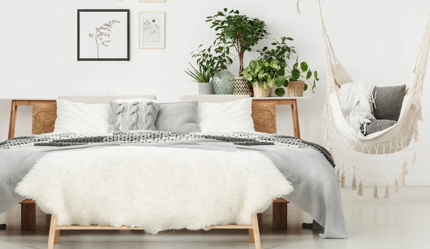 Bright white bedroom featuring layered knit bedding, a cluster of indoor plants, and a hanging macrame chair.